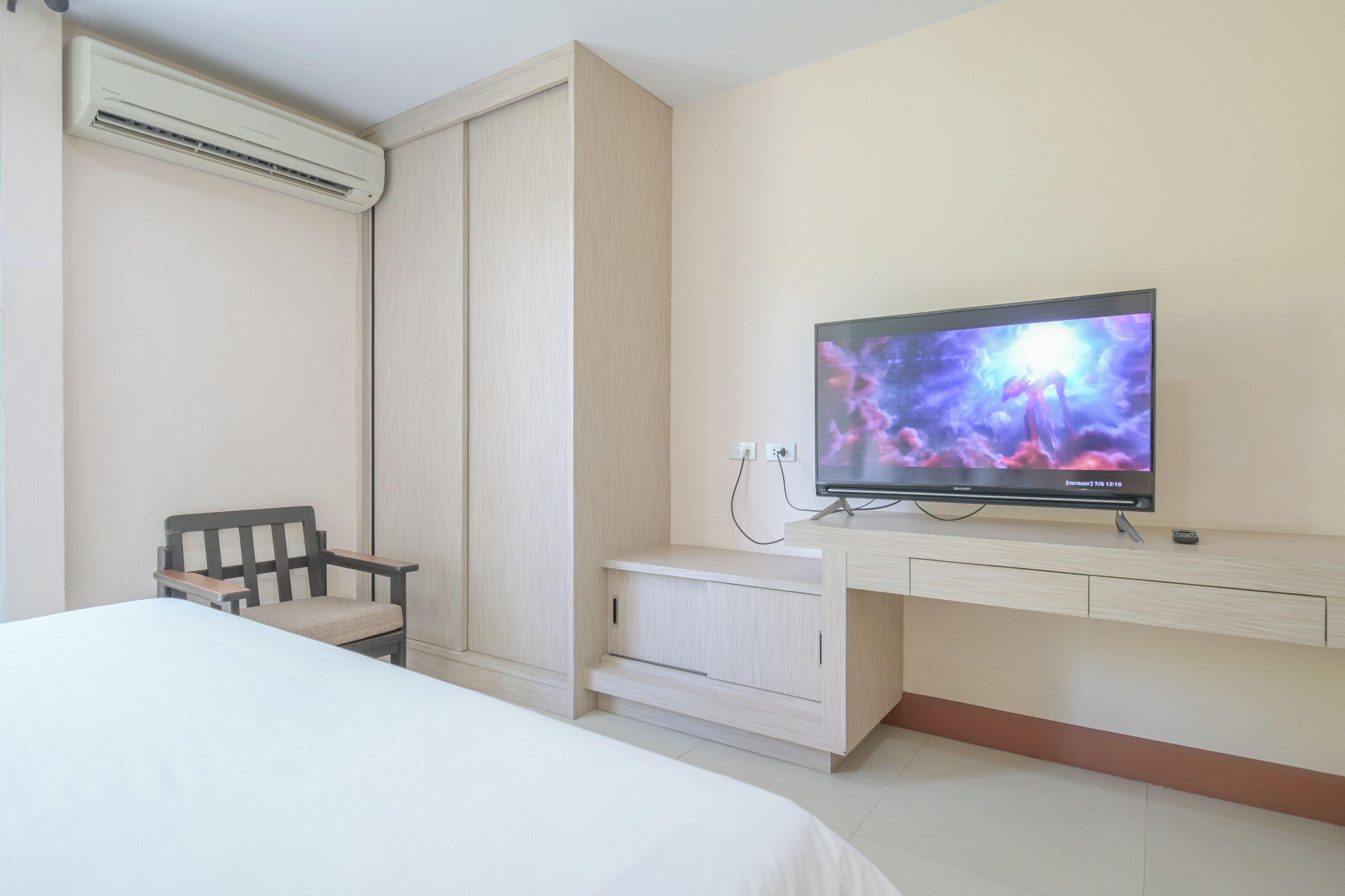 A hotel room with a bed, a TV mounted on the wall, a chair, and a wardrobe.