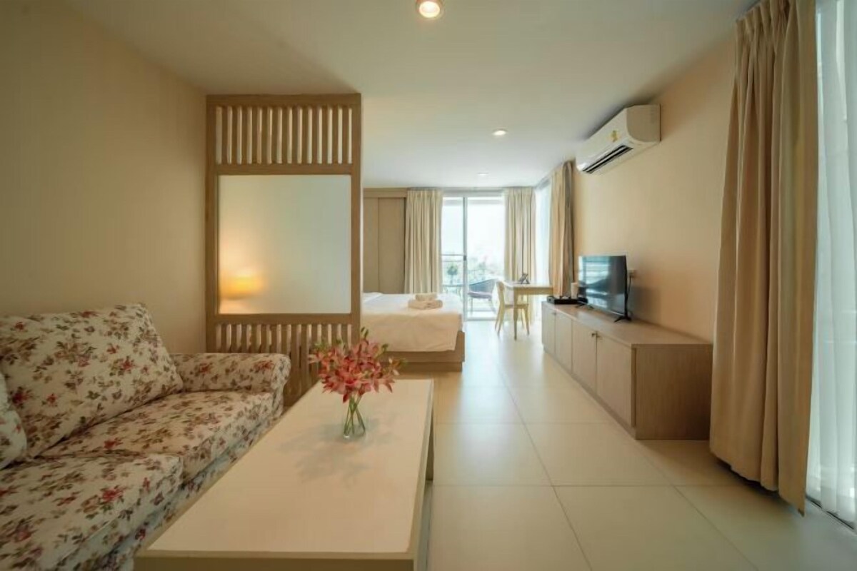 A hotel room with a sofa, a bed, a TV, a desk, and a large window.