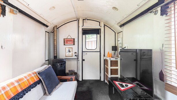 A compact interior with a sofa, a small table, a television, and a door leading outside. - Tiny House Train-Eco Stay (Upper Hutt)