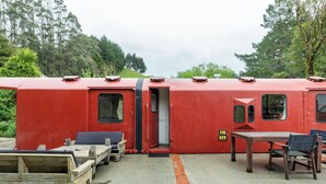 A red train car with a door, a small table, and a chair. - Tiny House Train-Eco Stay (Upper Hutt)
