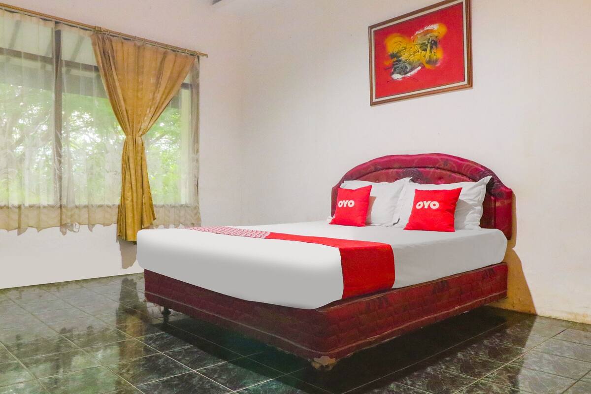 Een hotelkamer met een bed, gordijnen, een schilderij en een betegelde vloer.