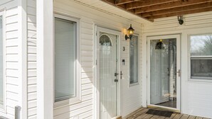 A white house with a wooden porch, a glass door with a number '3' above it, and a small light fixture on the wall. - Charming KY Lake Condo Short Walk to Lake (Gilbertsville)