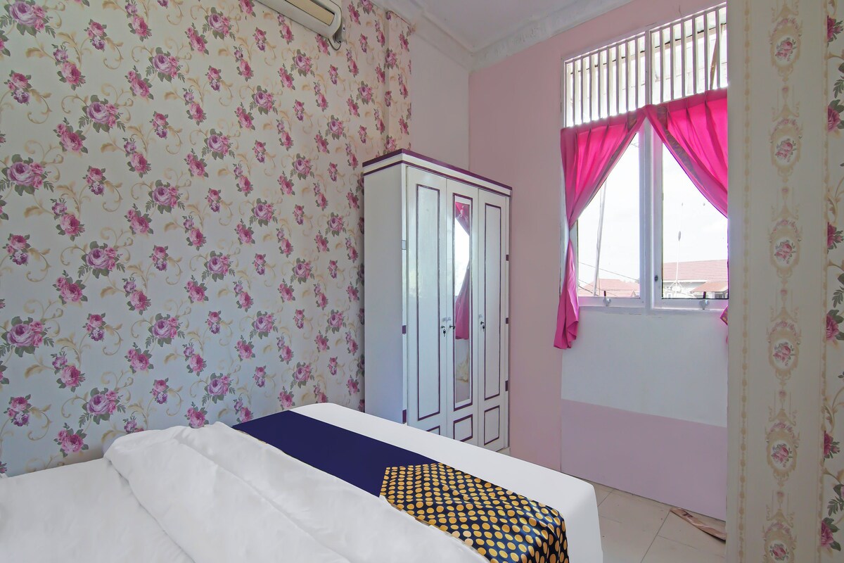 Ein Zimmer mit floraler Tapete, einem Bett mit gemustertem Überwurf, einem Kleiderschrank und einem Fenster mit Vorhängen.
