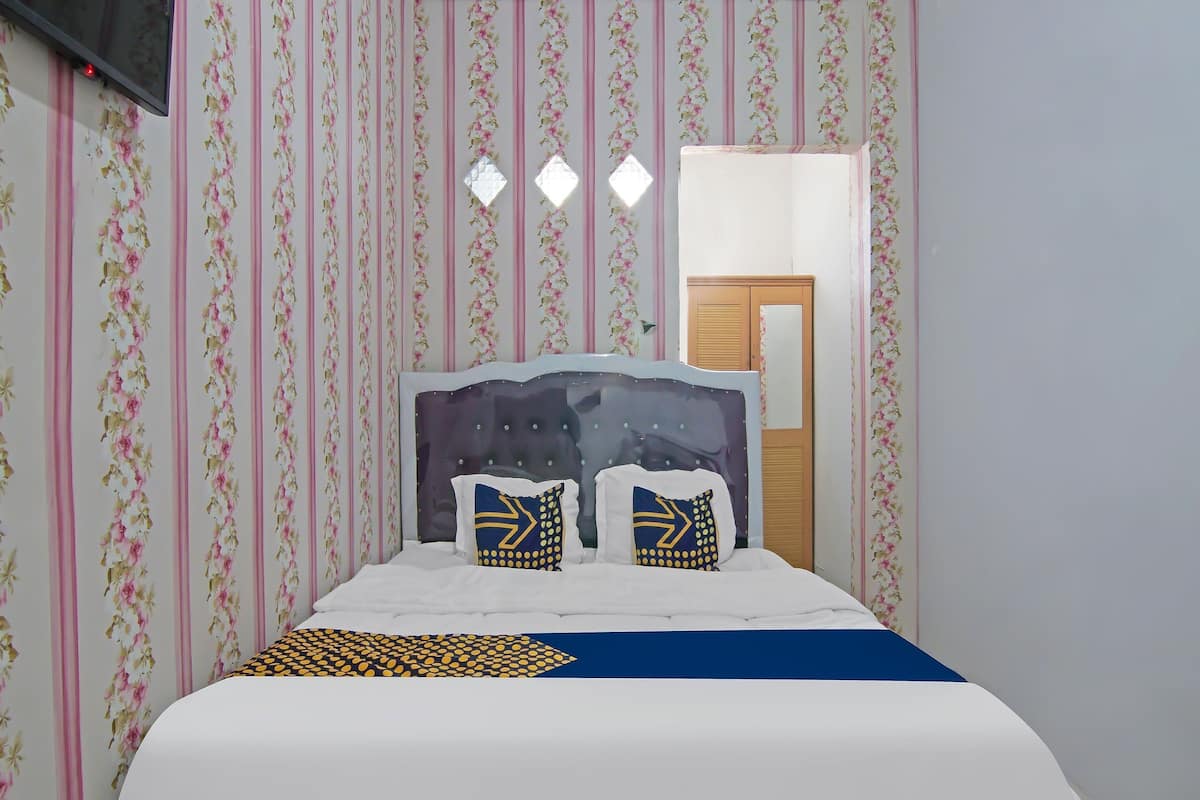 Ein ordentlich bezogenes Bett mit einem gemusterten Überwurf, einem Kopfteil mit dekorativen Kissen und einer Wand mit floralem, vertikalem Wandpapier.