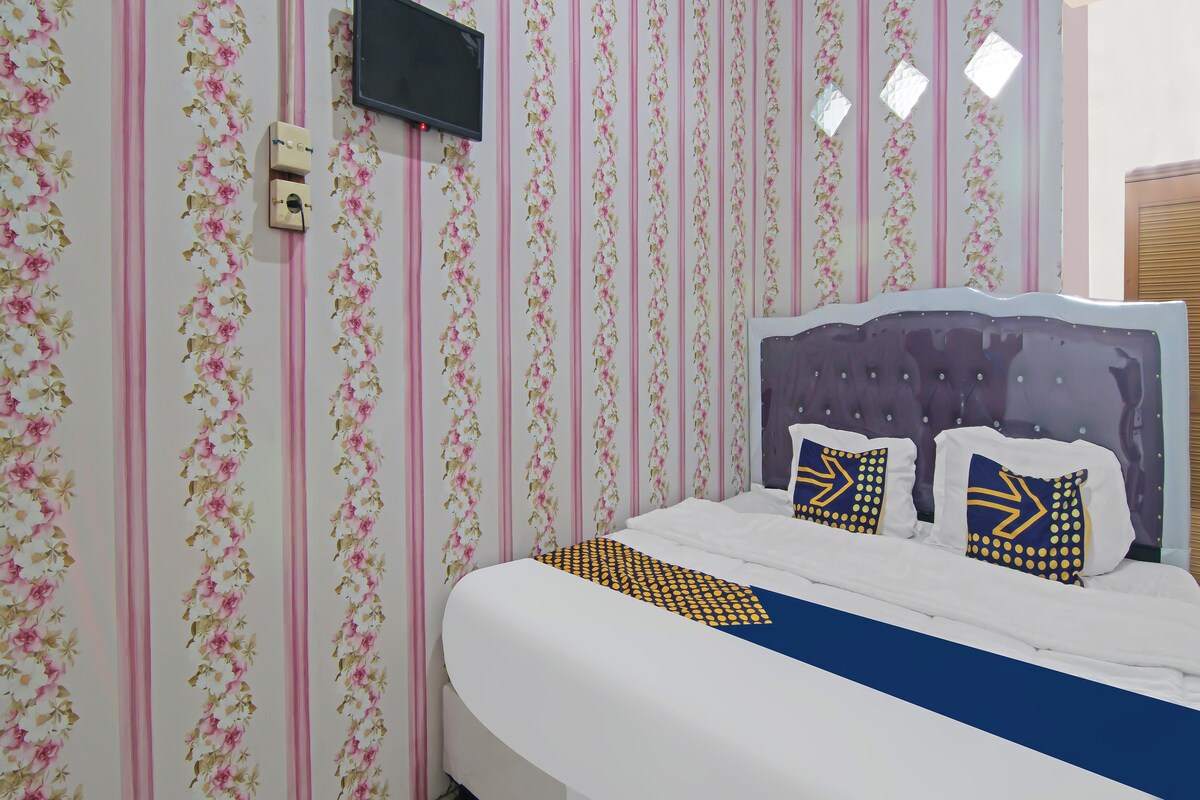 Une chambre à coucher avec un lit, un téléviseur fixé au mur et une fenêtre avec des stores.