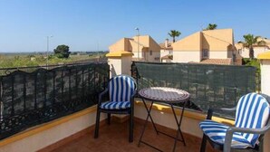 A balcony with two striped chairs and a small round table, overlooking a residential area with houses and greenery. - CH Isamar Park Doña Pepa (Ciudad Quesada) (Ciudad Quesada)