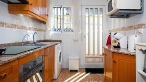 A compact kitchen with wooden cabinets, a built-in oven, a washing machine, and a microwave. - CH Isamar Park Doña Pepa (Ciudad Quesada) (Ciudad Quesada)