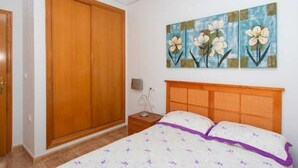 A bedroom with a wooden wardrobe, a bed with a purple accent, and a floral painting on the wall. - CH Isamar Park Doña Pepa (Ciudad Quesada) (Ciudad Quesada)