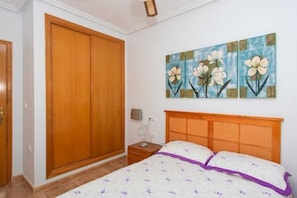 Une chambre avec une armoire en bois, un lit agrémenté de touches violettes et un tableau floral accroché au mur.