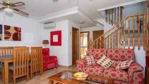 A living room with a wooden staircase, a red sofa, and a dining area with wooden chairs and a table. - CH Isamar Park Doña Pepa (Ciudad Quesada) (Ciudad Quesada)