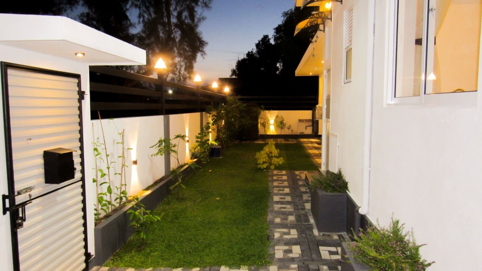 Una casa moderna con un porche cubierto, un pequeño jardín y un sendero que lleva a la entrada.