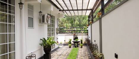 A covered outdoor area with a brick pathway, potted plants, and a water feature.