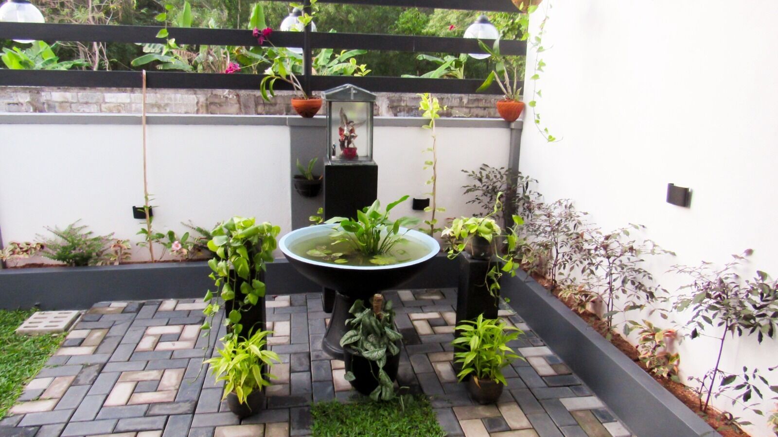 Pátio com um elemento central de água, rodeado por vasos de plantas e uma mesa preta.
