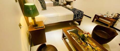 A hotel room with a bed, bedside table with a lamp, a small table with a vase, a chair, and a television on the wall.