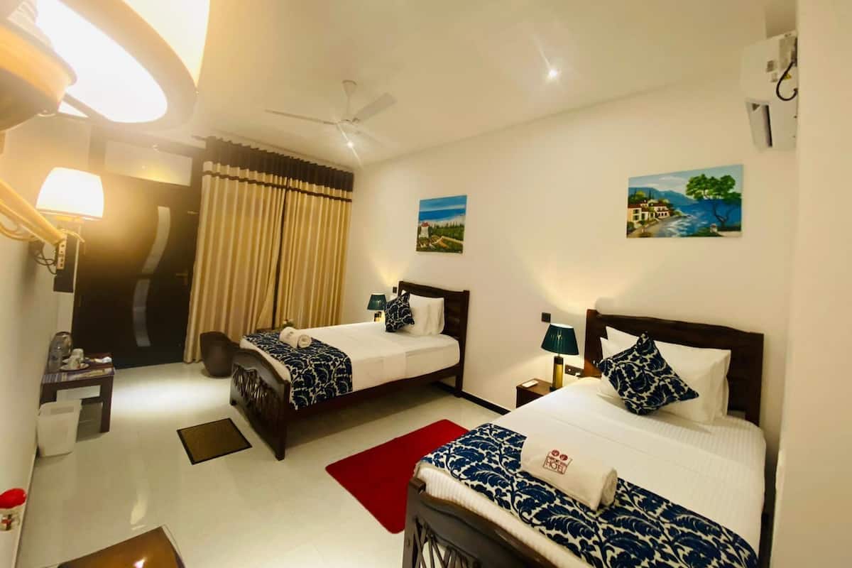 Ein Hotelzimmer mit zwei Betten, einem Deckenventilator, einem Nachttisch, einer Lampe und Bildern an den Wänden.