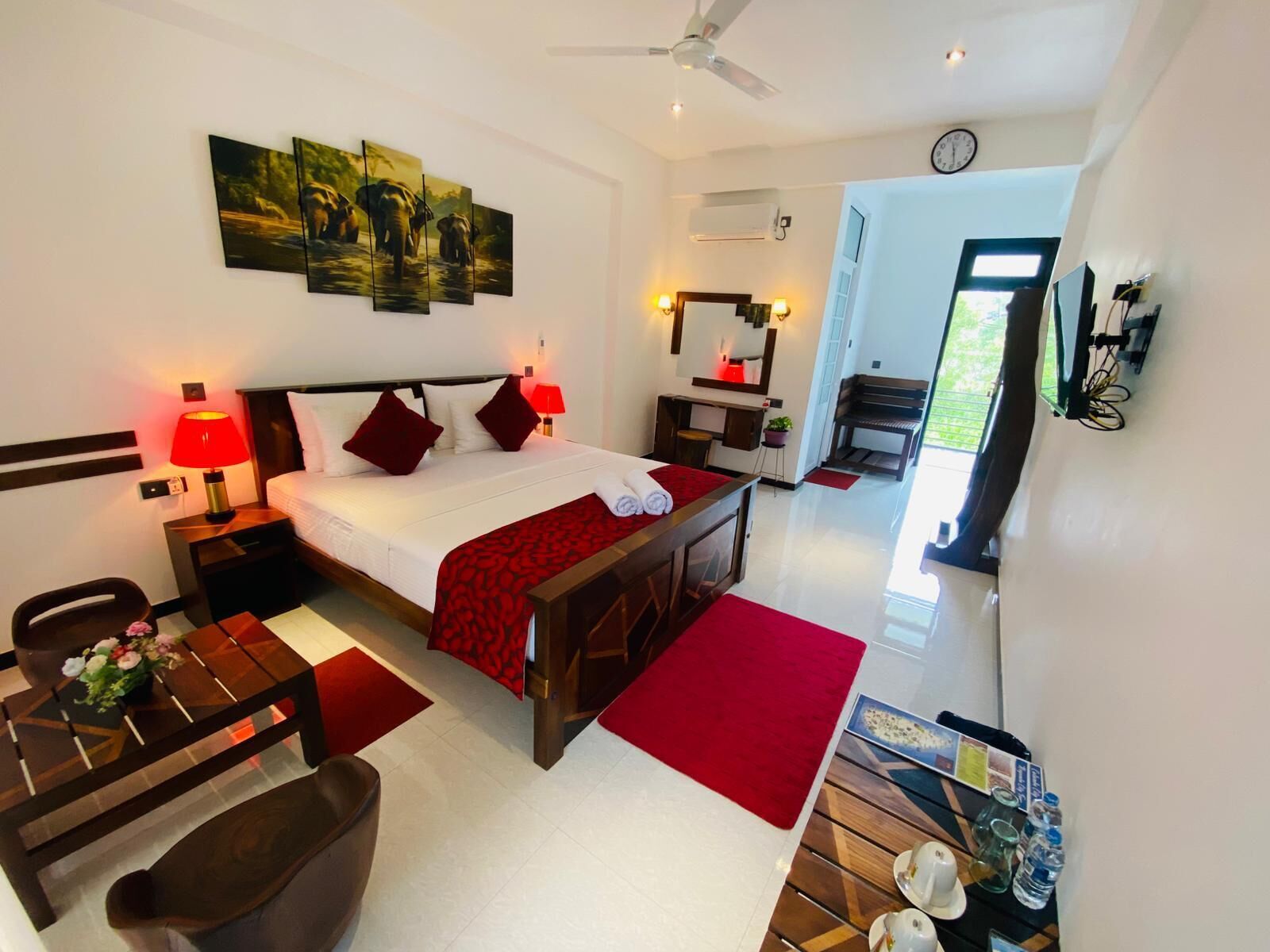 A hotel room with a bed, bedside lamps, a desk with a chair, a piano, and a large window.