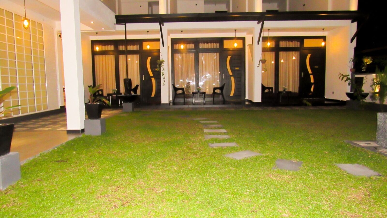 A hotel entrance with a well-maintained lawn, stone pathway, and modern doors with curtains.