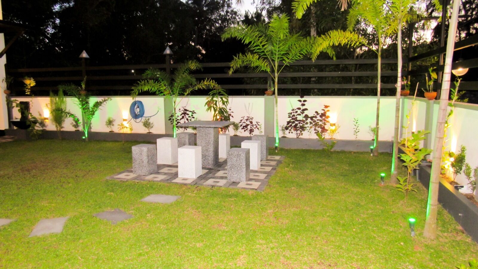 A well-maintained garden area with a central stone structure, surrounded by neatly trimmed grass and various plants.