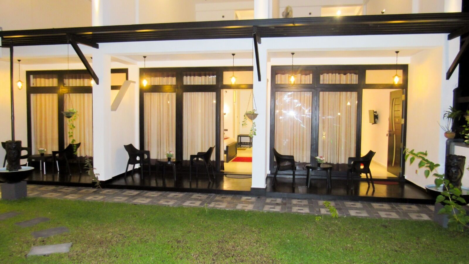 A hotel with a covered outdoor seating area, a small pool, and a well-maintained lawn.
