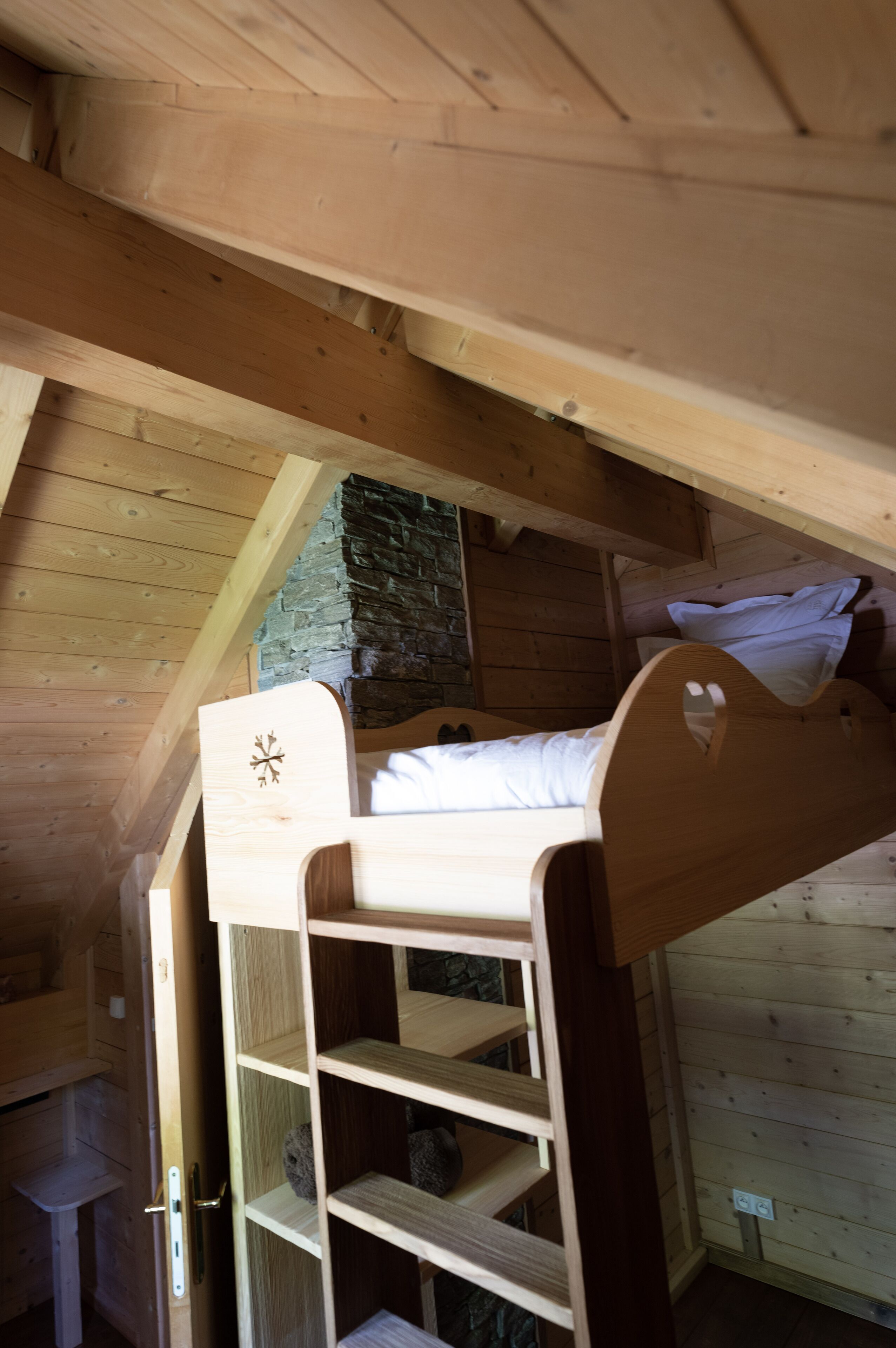 A wooden bunk bed with a ladder, a stone wall, and a wooden ceiling in a cabin-style room.