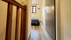 A narrow hallway with wooden flooring leading to a bedroom with a bed.