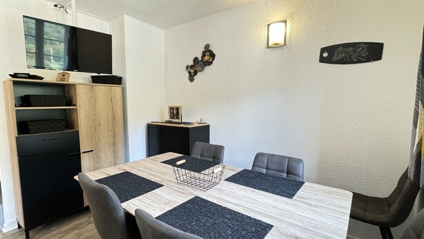 A dining area with a wooden table, four grey chairs, a black cabinet, and a small shelf with decorative items.