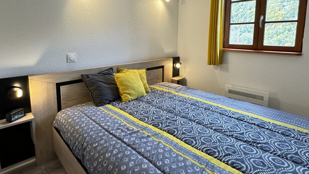 Une chambre à coucher avec un lit, des lampes de chevet, une fenêtre avec des rideaux et une vue sur la verdure à l’extérieur.