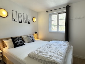 A neatly made bed with white bedding, a headboard with a light fixture, and a window with curtains.