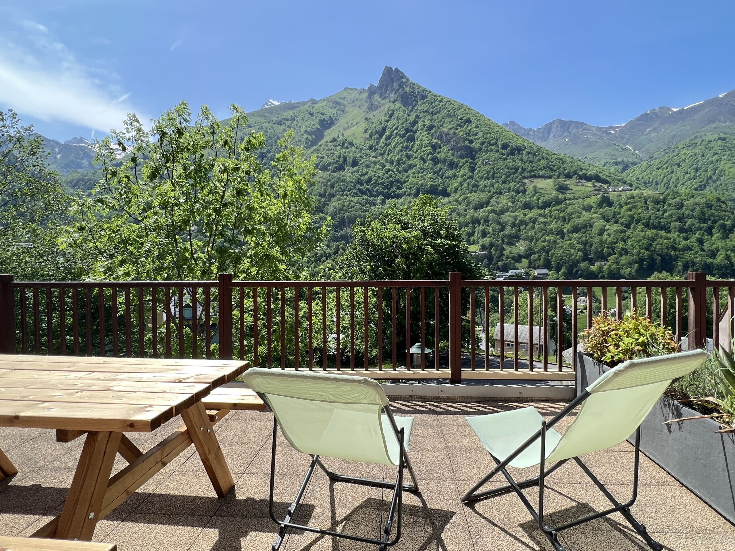 A wooden table and two chairs on a balcony with a view of a mountain range.