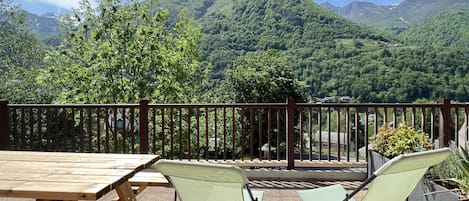 A wooden table and two chairs on a balcony with a view of a mountain range.