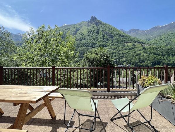 A wooden table and two chairs on a balcony with a view of a mountain range.