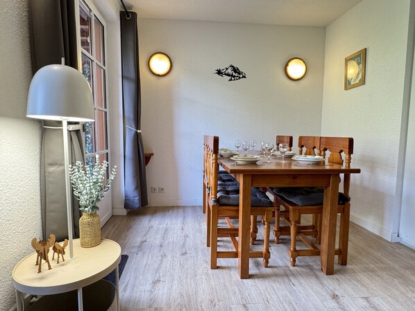Un comedor con una mesa de madera preparada para cuatro, dos luces fijadas a la pared y una lámpara sobre una mesita auxiliar.