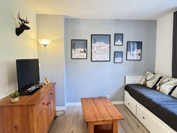 A room with a bed, a TV on a wooden cabinet, a small table, and wall-mounted pictures.