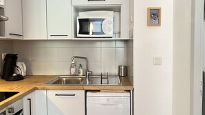 A modern kitchen with white cabinets, a microwave, a sink with a faucet, a coffee maker, and a dishwasher.