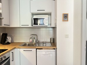 Una cocina moderna con gabinetes blancos, microondas, lavamanos con grifo, cafetera y lavavajillas.