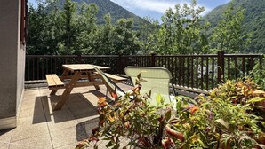 A balcony with a wooden table and chairs, a view of a mountain range, and a railing.