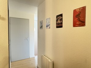 Un pasillo con una puerta blanca, un radiador y tres carteles en la pared.