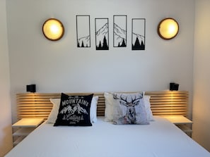 Una cama con dos almohadas, una pared con cuatro cuadros enmarcados y dos lámparas de pared.