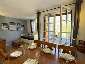 A dining area with a table set for four, a sofa, and a window with curtains. - Duplex + terrasse panoramique.Parking.Piscine été (Cauterets)