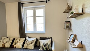 A bedroom with a bed, a window with curtains, and wall-mounted shelves with decorative items.