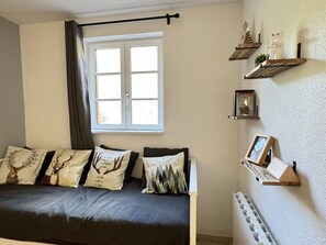 Un dormitorio con cama, ventana con cortinas y estantes en la pared decorados con objetos.