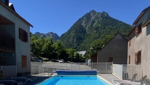 A swimming pool with lounge chairs, surrounded by buildings and a mountain backdrop. - T3 rénové avec balcon, vue montagne et Parking. (Cauterets)
