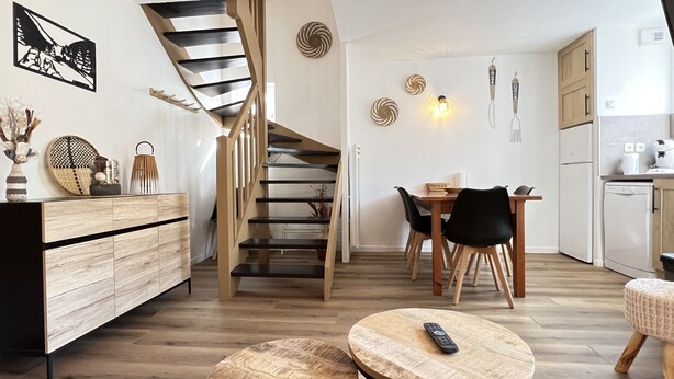 A modern kitchen with wooden cabinets, a dining area with a table and chairs, and a spiral staircase. - T3 rénové avec balcon, vue montagne et Parking. (Cauterets)