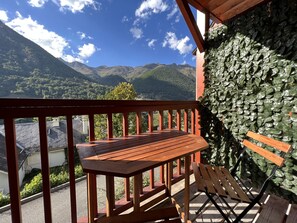 Um deck de madeira com um banco e uma mesa, com vista para uma paisagem montanhosa sob um céu limpo.