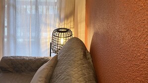 A room with a bed, a wall-mounted light fixture, and a window with curtains. - T3 rénové avec balcon, vue montagne et Parking. (Cauterets)
