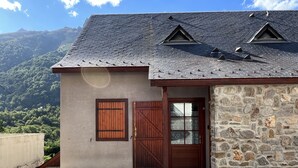A building with a stone facade, a wooden door, and a view of a mountainous landscape. - T3 rénové avec balcon, vue montagne et Parking. (Cauterets)