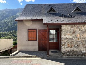 Uma casa de dois andares com fachada de pedra, porta de madeira e um pequeno alpendre.