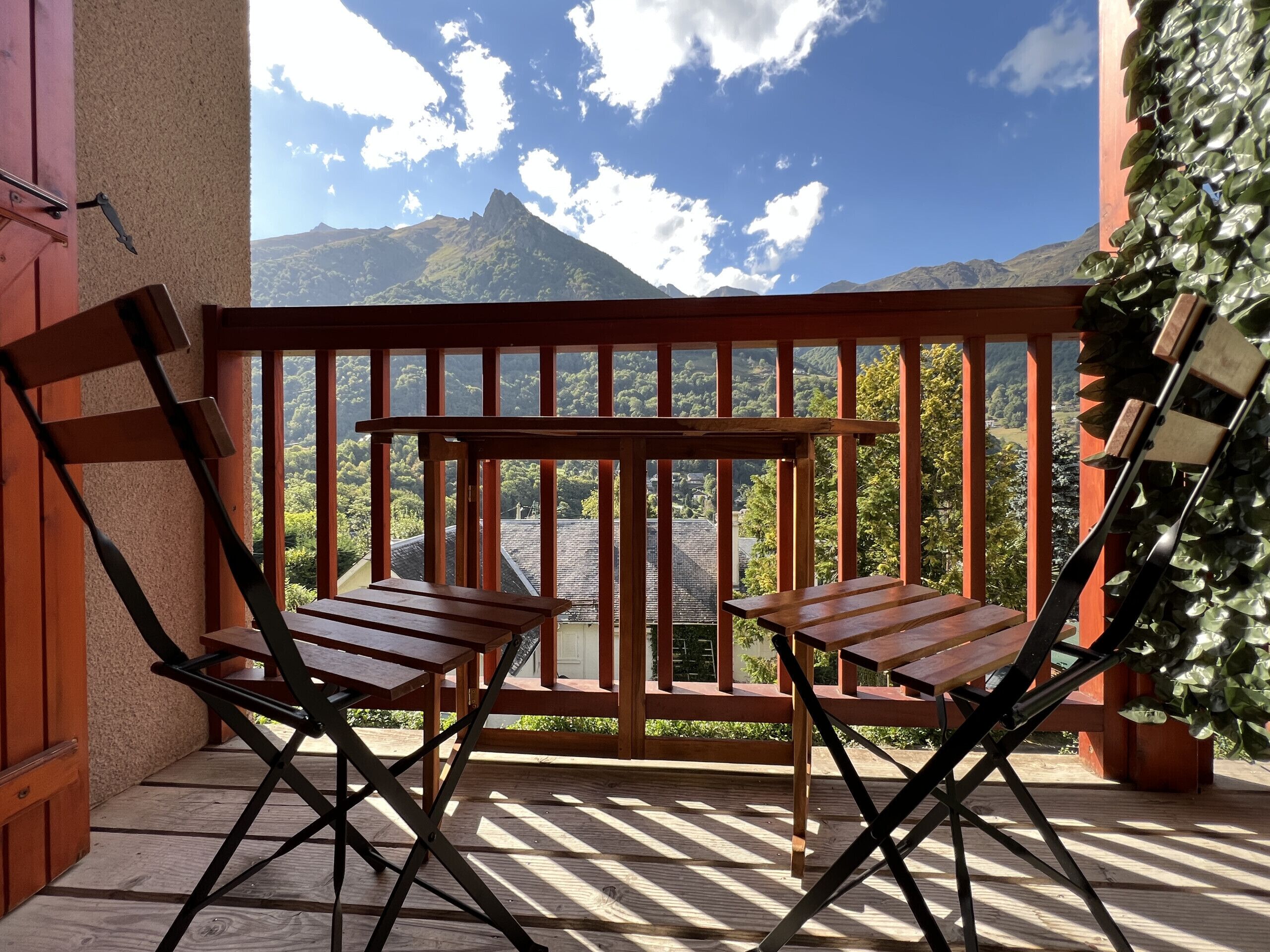 Una terraza de madera con dos sillas y una mesa, con vistas a un paisaje montañoso.