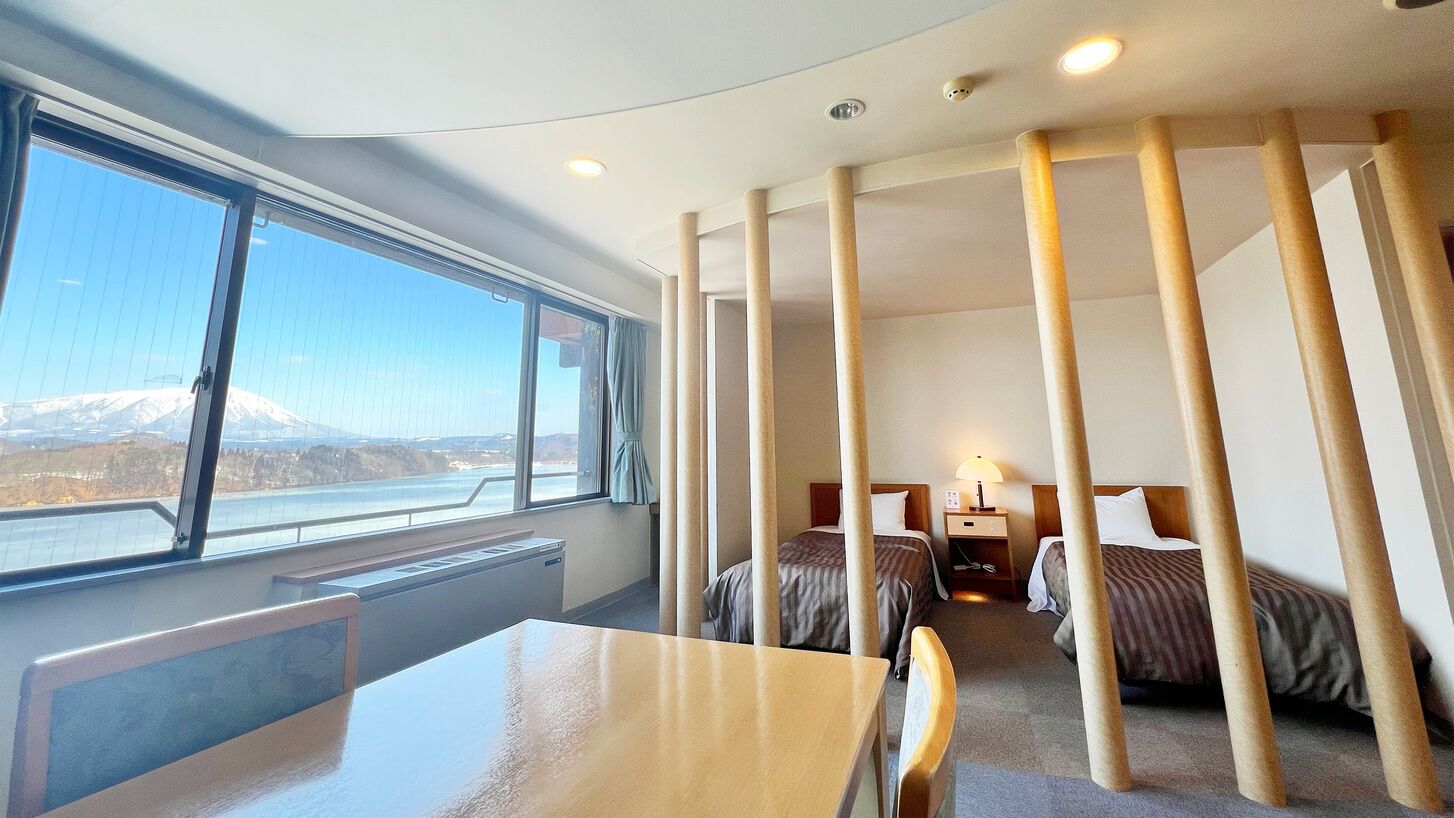 A hotel room with a large window, two beds, a desk, and a chair.