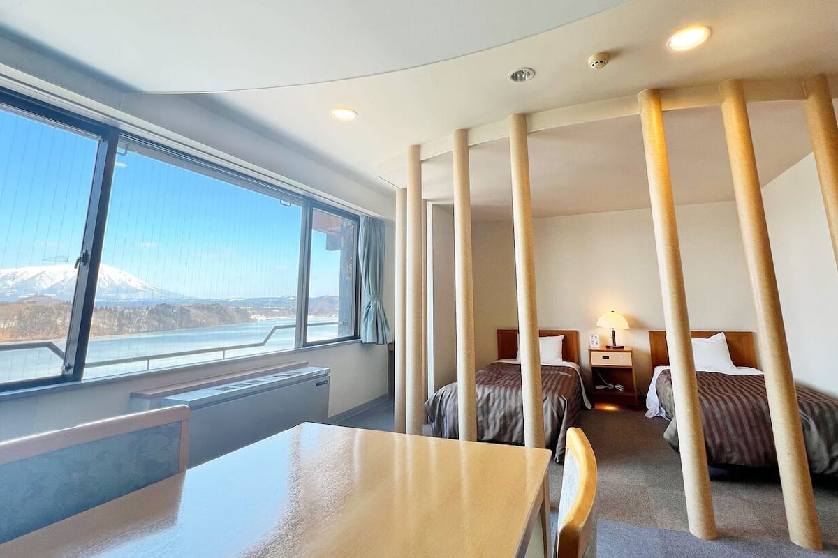 A hotel room with a large window, two beds, a desk, and a chair.